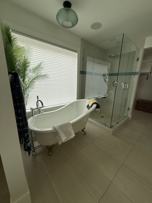 A beautiful tiled bathroom with claw foot bathtub and standup glass shower that is so clean you can see the reflection of the window in it.