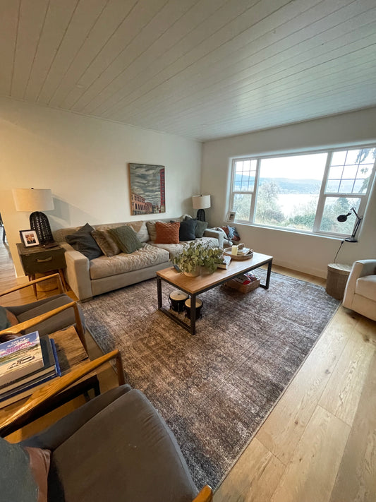 A picture of a living room with hardwood floors and an area rug with a coffee tabel, couch and two chairs all cleaned to perfection with a view out the newly cleaned window.